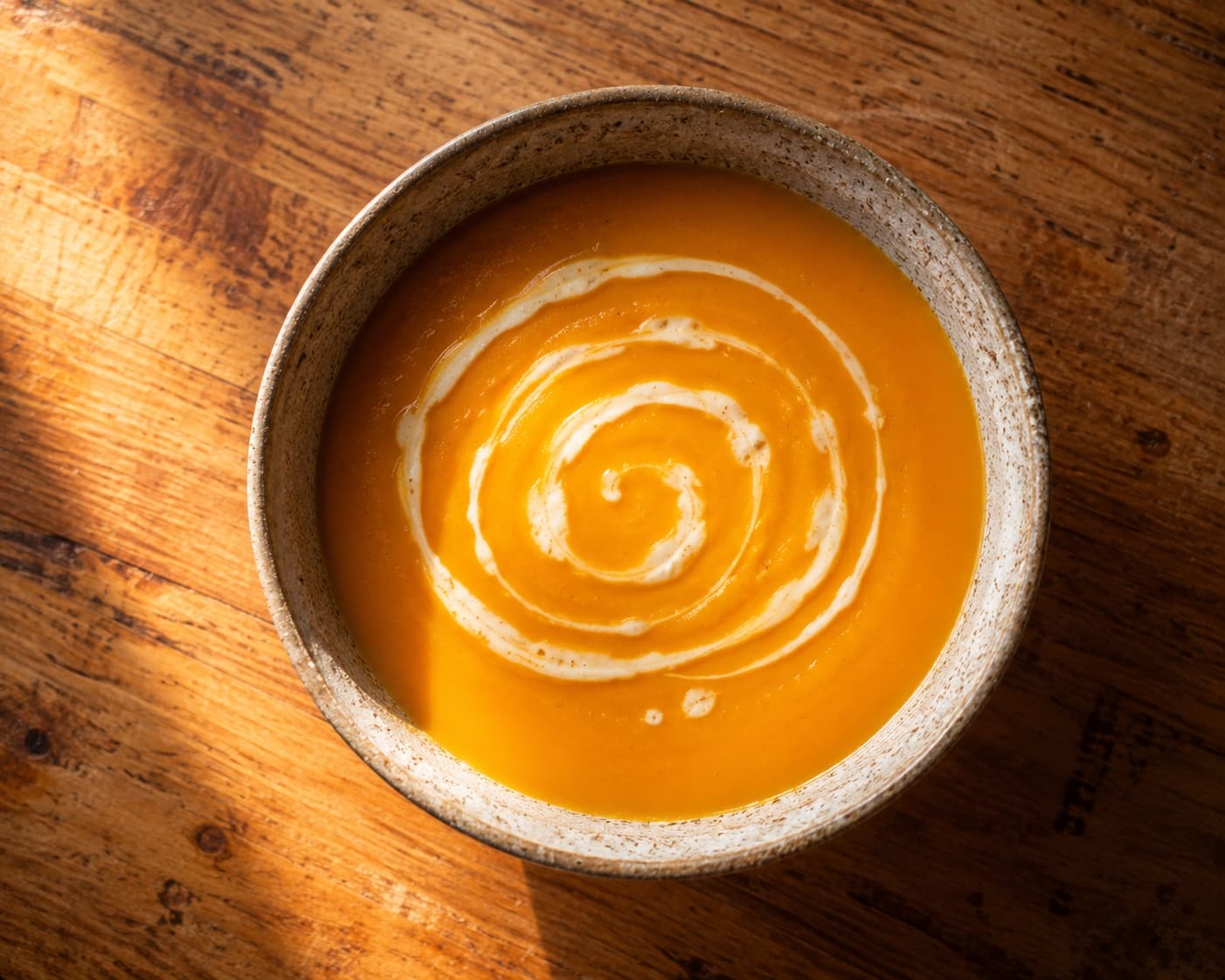 Crema de zapallo con un remolino de crema, en un bowl de cerámica sobre una mesa de madera